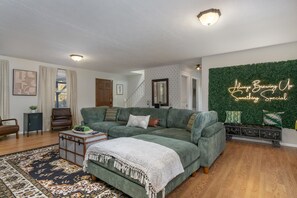 Ein modernes Wohnzimmer mit einem grünen Sofa, einem gemusterten Teppich und einer Wand mit einer Neonreklame.