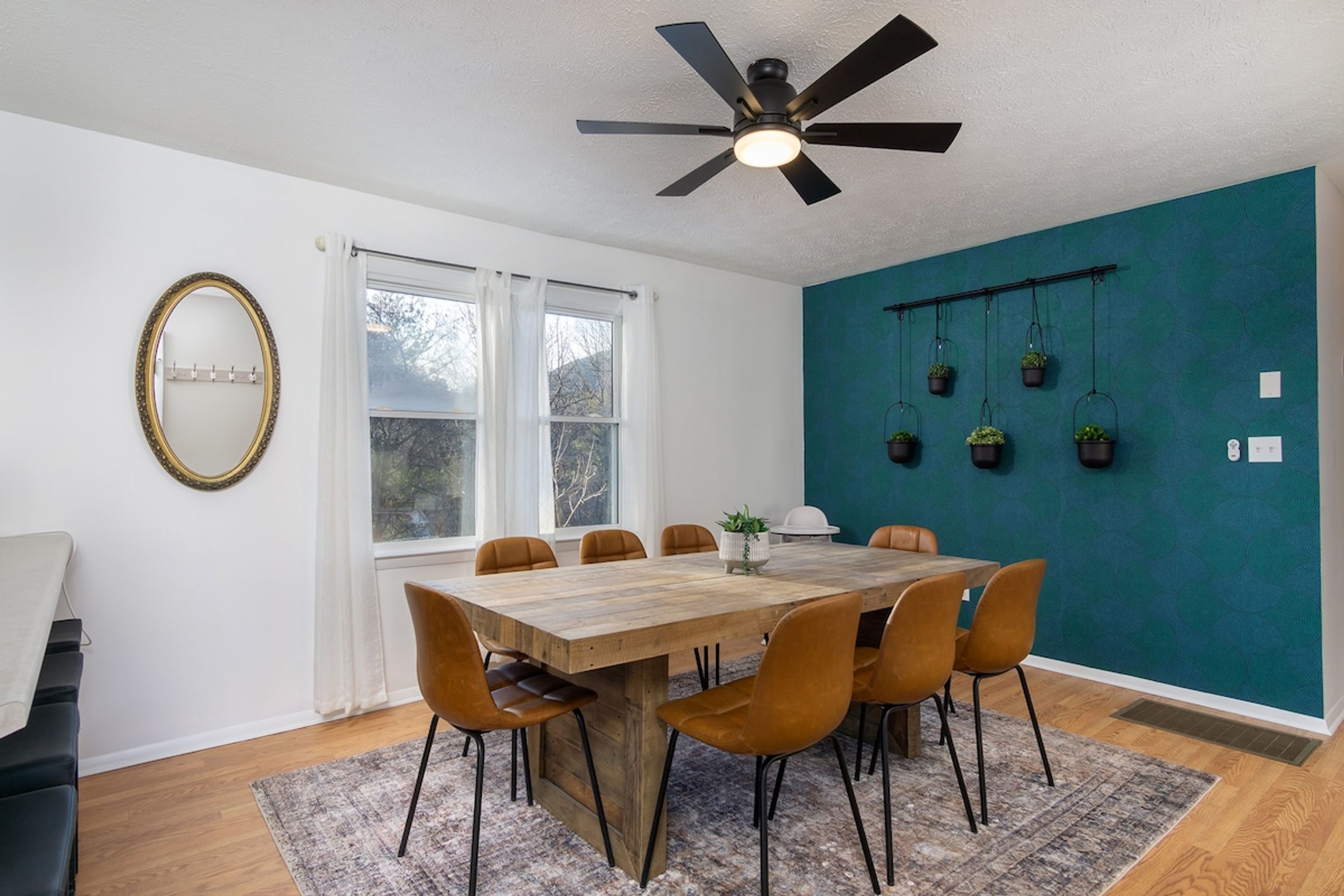 Un coin repas avec une table et des chaises en bois, un ventilateur de plafond et un mur d’accent de couleur turquoise agrémenté de jardinières suspendues.