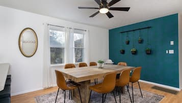 Un coin repas avec une table et des chaises en bois, un ventilateur de plafond et un mur d’accent de couleur turquoise agrémenté de jardinières suspendues.