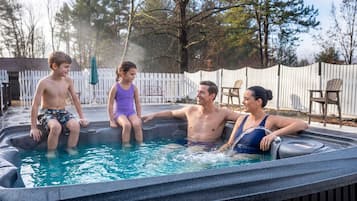 Une famille de quatre personnes dans un jacuzzi, avec une clôture blanche et des arbres en arrière-plan.