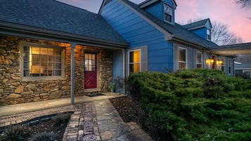 Une maison à deux étages avec une façade en pierre, une porte rouge et un chemin en pierre menant à l’entrée.