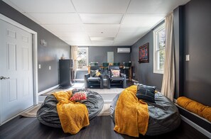 Ein modernes Wohnzimmer mit einer Couch, einem Couchtisch und einem Fernseher. Eine Tür führt in einen anderen Raum, ein Fenster mit Vorhängen.
