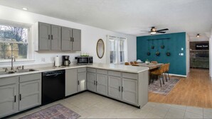 Una cucina moderna con mobili grigi, una lavastoviglie e un forno a microonde. C'è un'area pranzo con un tavolo e sedie, e una parete d'accento color petrolio.