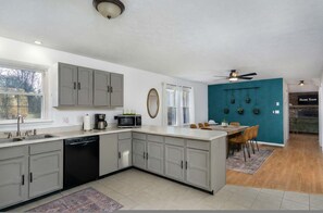 A modern kitchen with grey cabinets, a dishwasher, and a microwave. There's a dining area with a table and chairs, and a teal accent wall. - 15 Mins to DT Asheville Pool Hot Tub Game Room (Asheville)