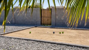 A courtyard with a gravel surface, a wooden gate, and a low wall. - The Palm Putt Heated Pool Golden Tee Bocce (Phoenix)