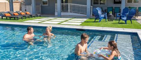 A swimming pool with a clear blue water surface, surrounded by a deck area with lounge chairs and a small patio with chairs and a table.