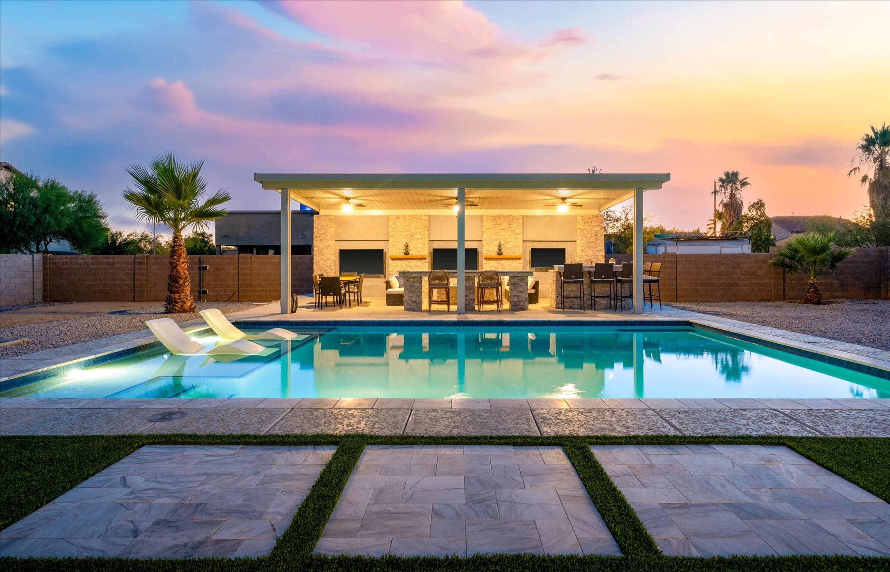 A modern outdoor pool area with lounge chairs, a covered seating area, and a stone wall.