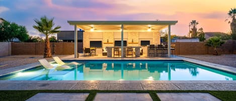 A modern outdoor pool area with lounge chairs, a covered seating area, and a stone wall.