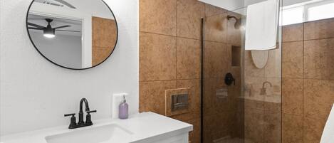A bathroom with a white vanity, a round mirror, a handheld showerhead, and a toilet.