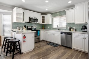 A modern kitchen with white cabinetry, stainless steel appliances, and a central island. - The Palm Putt Heated Pool Golden Tee Bocce (Phoenix)
