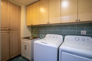 A compact laundry room with wooden cabinets, a stainless steel sink, and two white front-loading washing machines. - The Palm Putt Heated Pool Golden Tee Bocce (Phoenix)