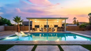 A modern outdoor pool area with lounge chairs, a covered seating area, and a stone wall. - The Palm Putt Heated Pool Golden Tee Bocce (Phoenix)