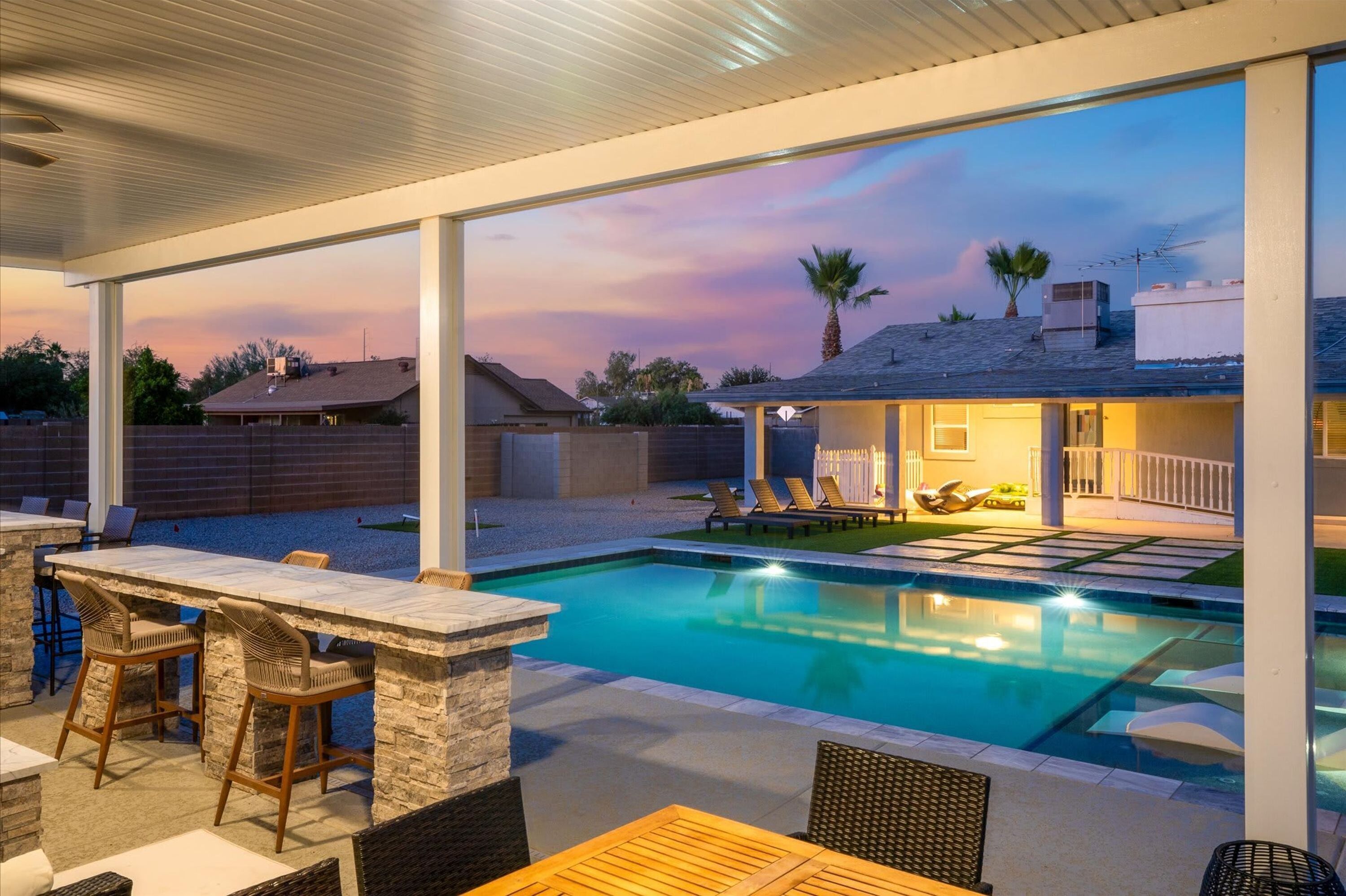 Uma área de piscina ao ar livre com um terraço coberto, assentos e vista para o pôr do sol.