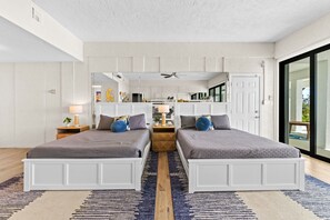 Um quarto moderno com duas camas, um espelho grande e uma cozinha visível através de uma porta aberta.