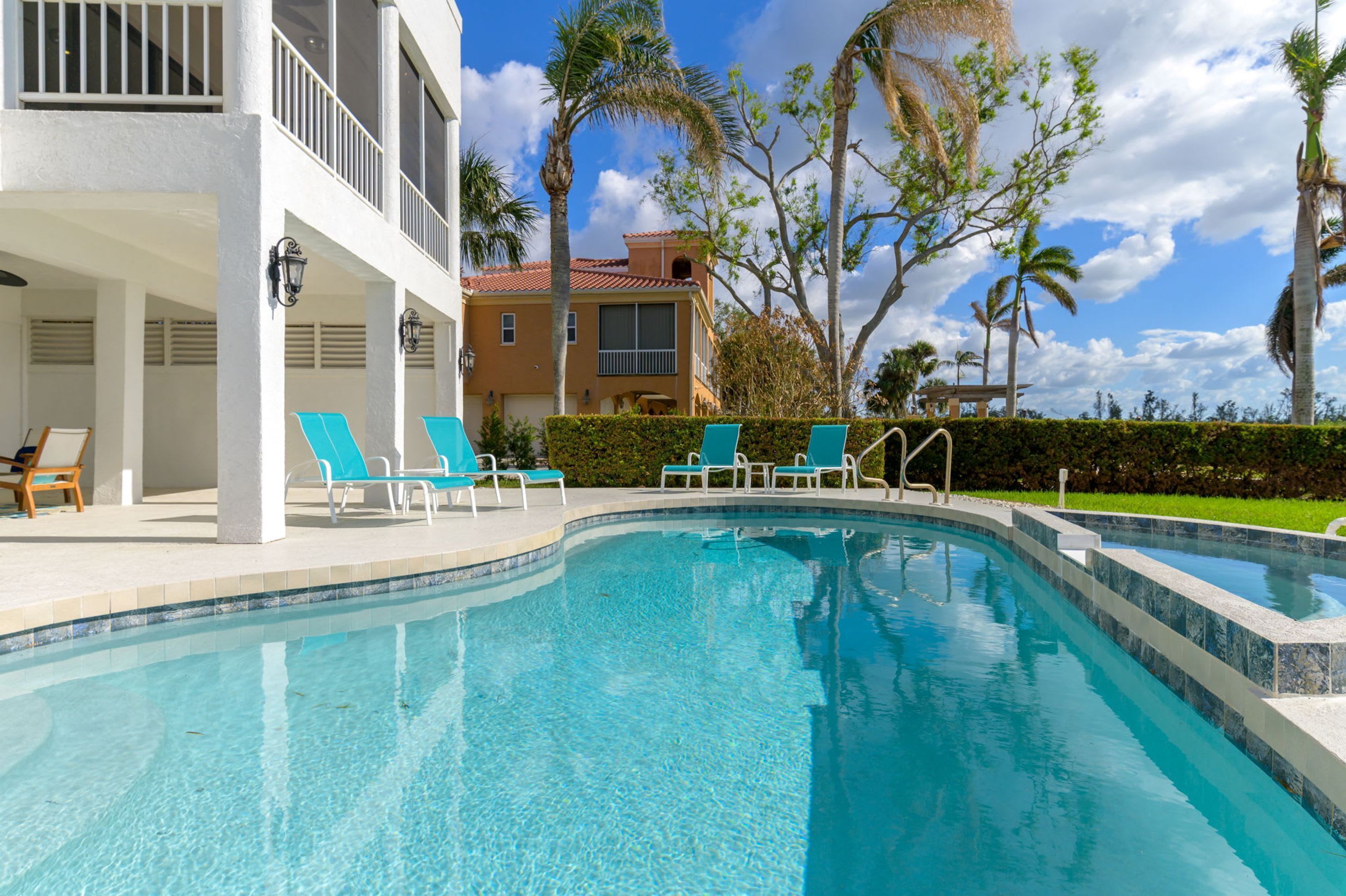 A swimming pool with blue chairs and a building with balconies.