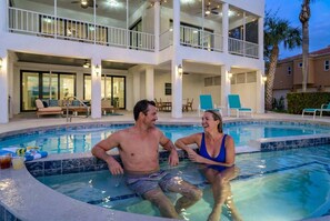 A swimming pool area with a two-story building, lounge chairs, and a palm tree. - Luxury Beachfront Retreat Pool Game Room Sleeps 16 (Bradenton)