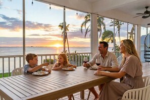 A family dining at a table with a view of the sunset over the ocean. - Luxury Beachfront Retreat Pool Game Room Sleeps 16 (Bradenton)