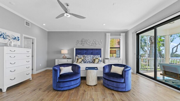 A modern living room with a ceiling fan, a white dresser, two blue armchairs, a coffee table, and a large window with a view. - Luxury Beachfront Retreat Pool Game Room Sleeps 16 (Bradenton)