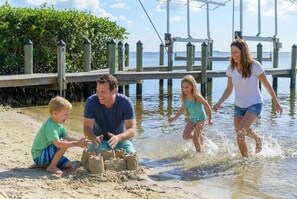 Eine vierköpfige Familie am Strand, mit einem hölzernen Steg und einem Sandspielplatz.