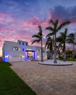 A modern building with a spacious paved courtyard, palm trees, and a well-lit entrance. - Luxury Beachfront Retreat Pool Game Room Sleeps 16 (Bradenton)
