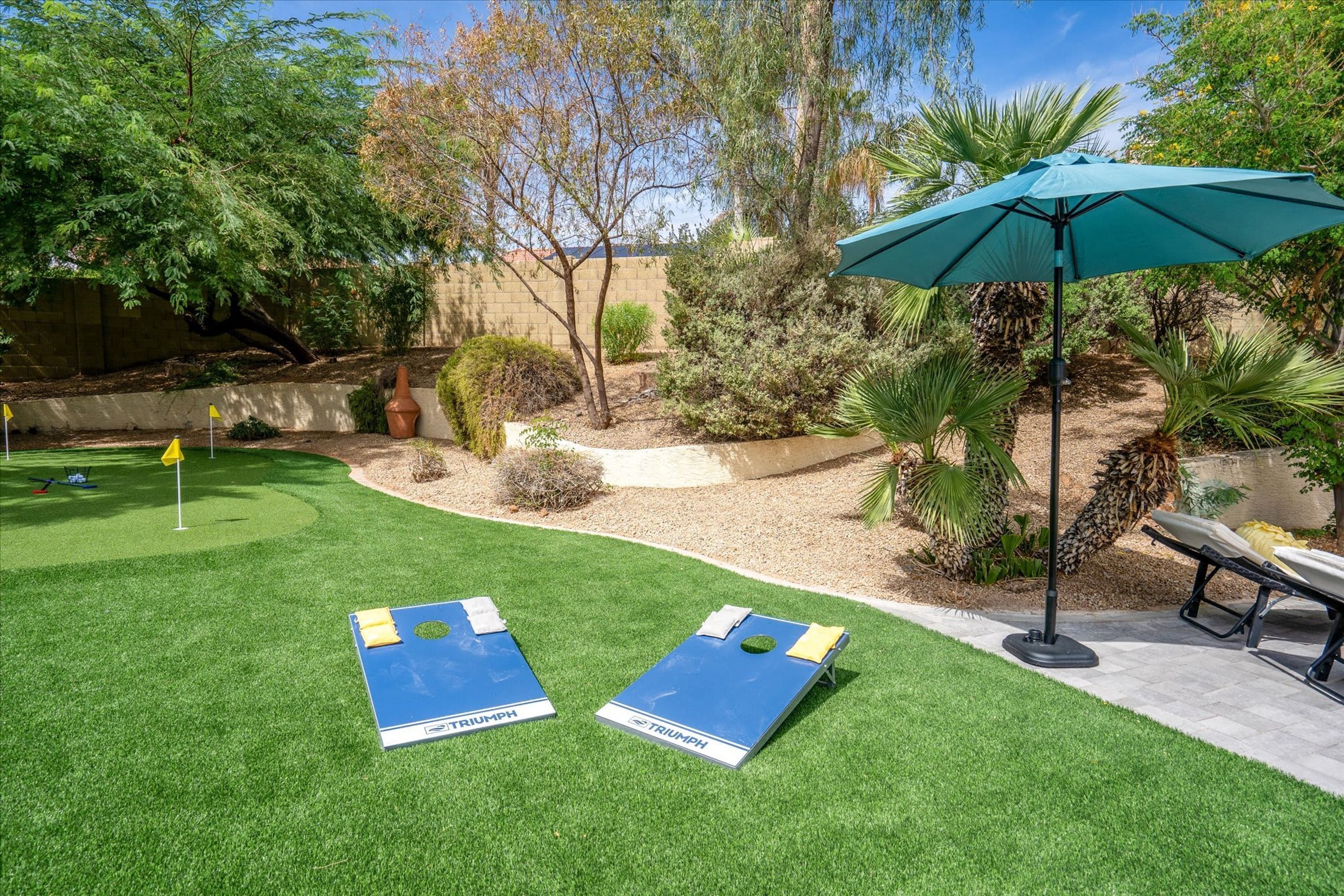 A backyard with artificial grass, two blue lounge chairs, a green umbrella, and a small pool area.