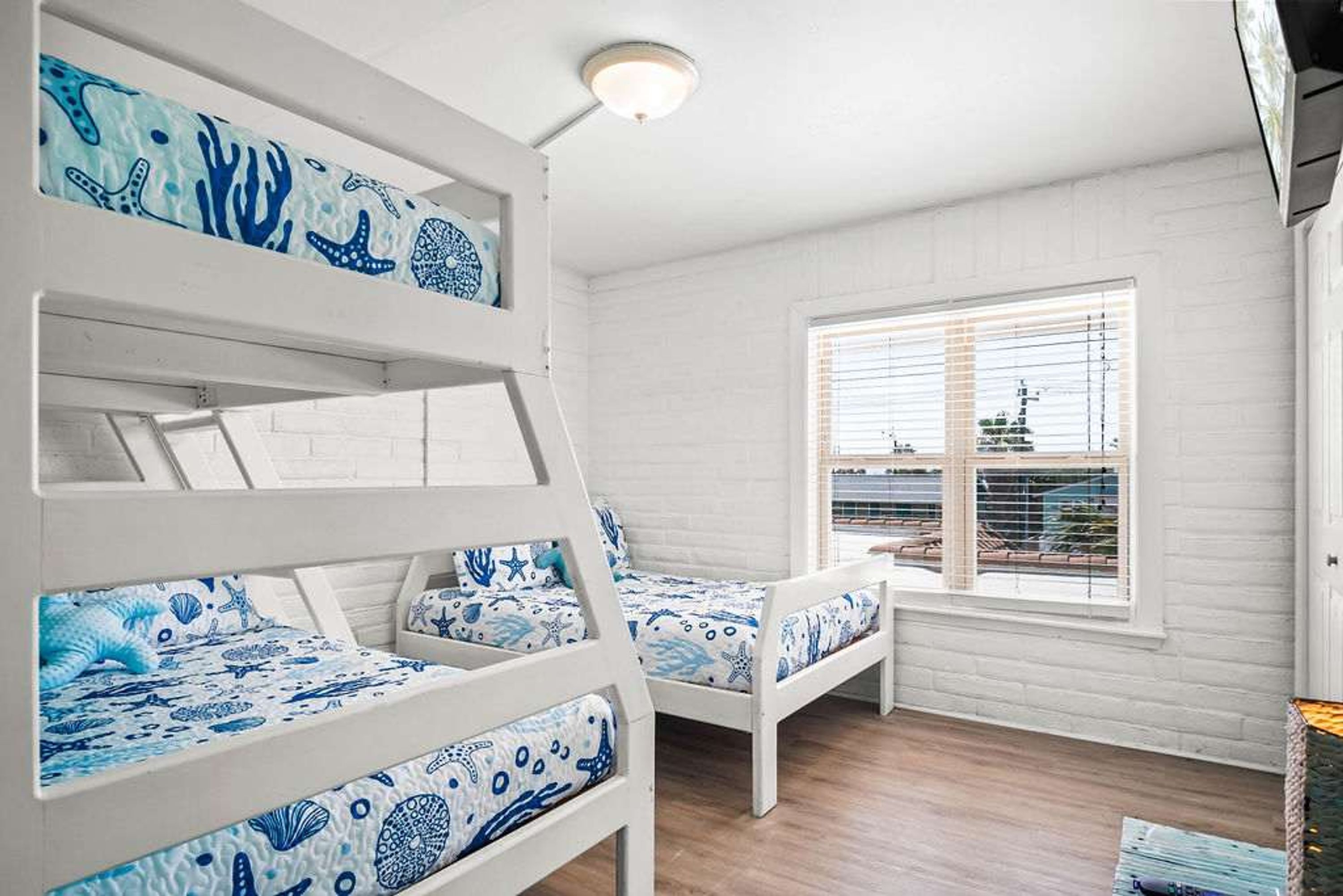 Une chambre avec des lits superposés, une fenêtre avec des stores et une vue sur un bâtiment à l’extérieur.