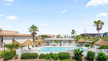 Una piscina con sillas de descanso y palmeras, rodeada por una valla y follaje.