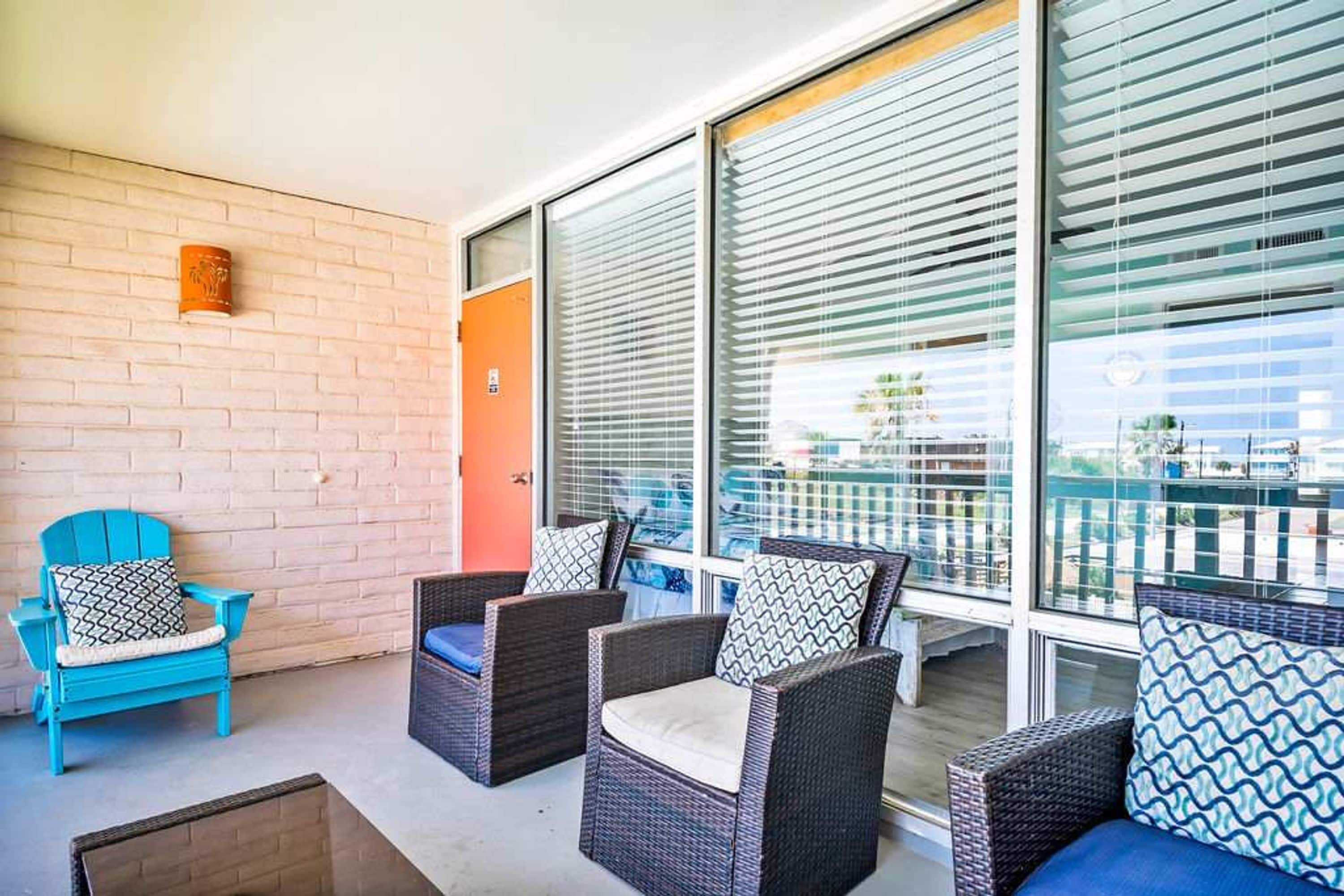 A balcony with wicker furniture, a blue chair, and a brick wall.