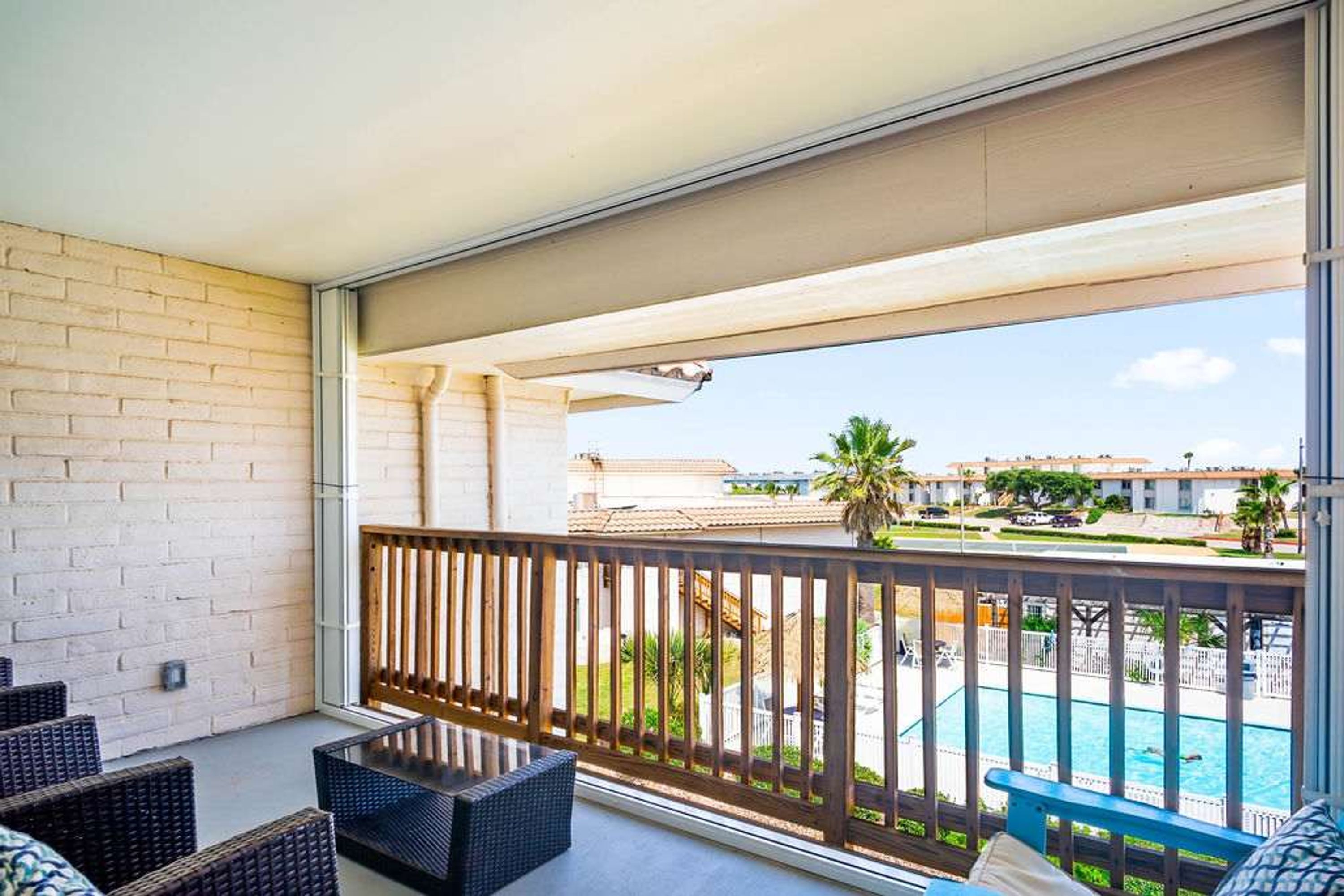 A balcony with wicker furniture, a view of a swimming pool, and a building in the background.