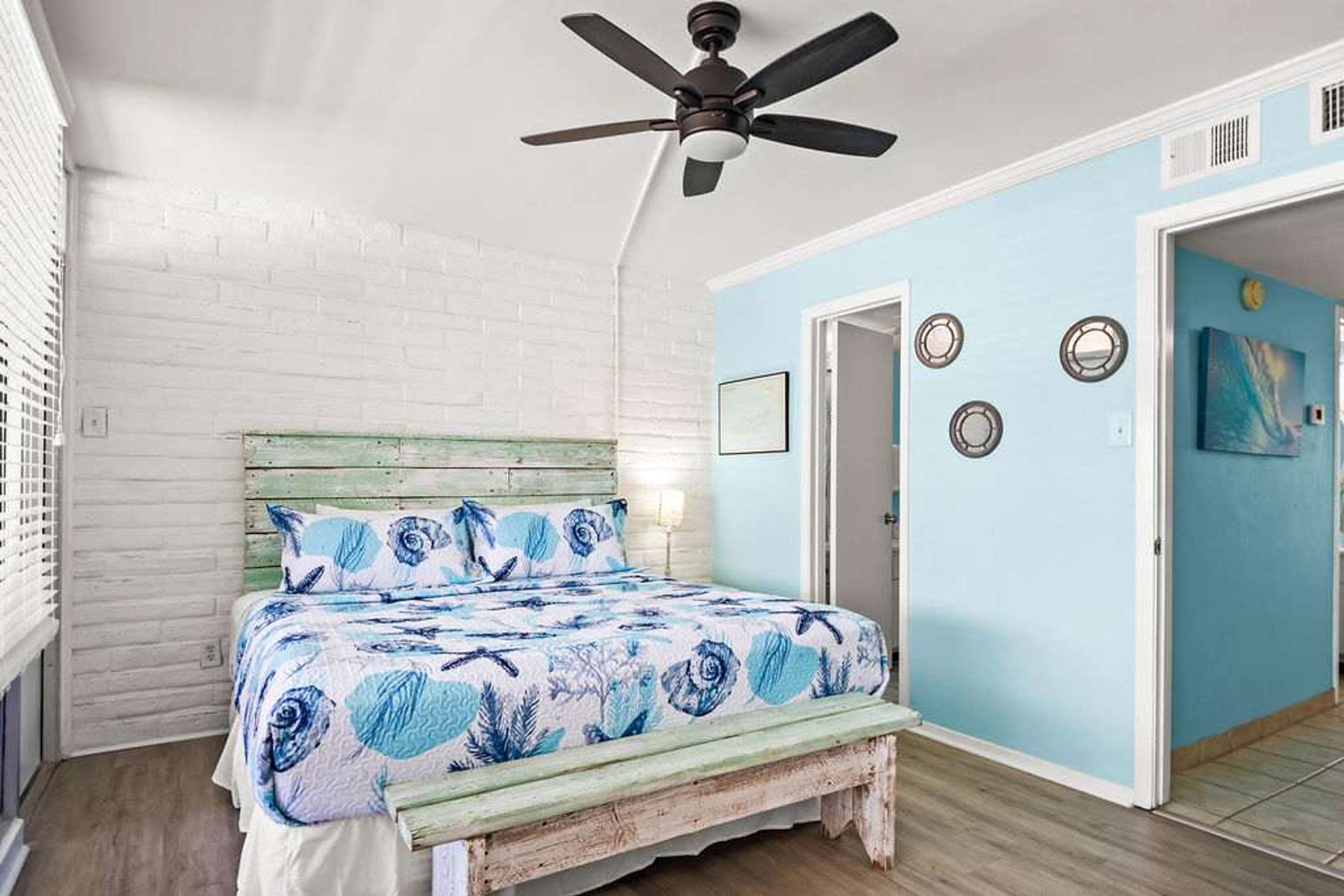 A bedroom with a bed, a ceiling fan, and a door leading to another room.