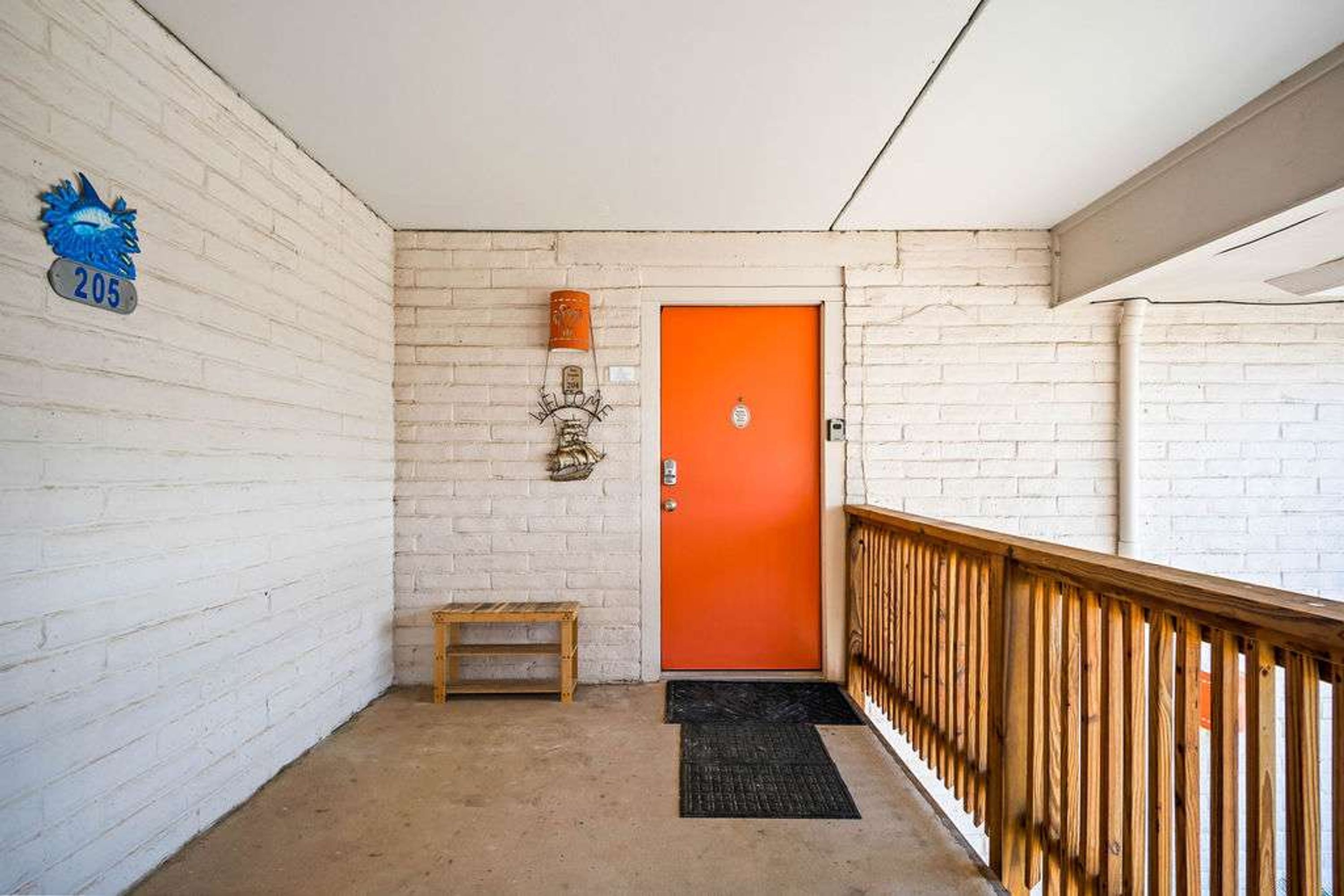 A corridor with a white brick wall, a wooden bench, a black mat, and a wooden railing.