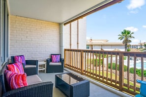Ein Balkon mit Korbmöbeln, einer weißen Backsteinmauer und Blick auf einen Pool und Palmen.