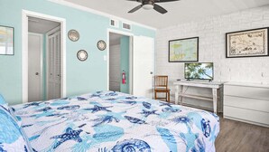 Un dormitorio con cama, escritorio, silla, ventilador de techo y pared de ladrillo blanco.