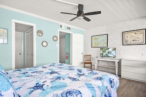 Ein Schlafzimmer mit Bett, Schreibtisch, Stuhl, Deckenventilator und einer weißen Ziegelwand.