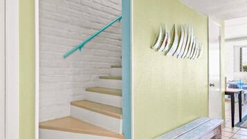 A staircase with white walls and teal accents, leading to a room with a green wall and a wooden bench.