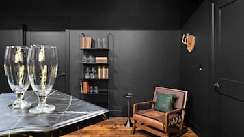 A room with a wooden floor, a black wall, a bookshelf, a leather chair, and a table with glasses.