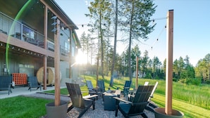 Een terras met Adirondack-stoelen en een vuurkuil, omgeven door een houten terras en een gebouw met een balkon.