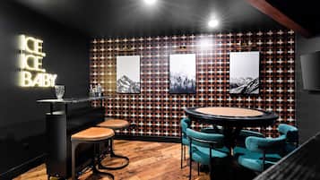 A bar area with a neon sign, wooden flooring, bar stools, a round table, and wall-mounted artwork.