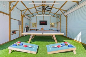 A room with a ceiling fan, a flat-screen TV, a table, and two bean bag chairs. - 4 Br Oasis Pool Tiki Hut Hot Tub Ping Pong Arcade (Seminole)
