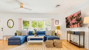 Una sala de estar con un sofá modular, una mesa de centro, una lámpara de pie, un televisor y un cuadro en la pared.