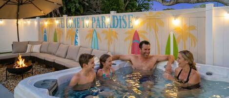 Un jacuzzi con un letrero que dice 'Welcome to Paradise', rodeado de mobiliario de exterior y palmeras.