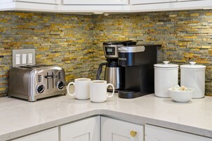 Una cocina moderna con protector contra salpicaduras de piedra, una cafetera, un tostador y dos tazas blancas sobre la encimera.