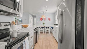 A modern kitchen with stainless steel appliances, a wooden dining table, and a view of the living area. - The Sandpiper Private Deck Bay Boat Parking (Port Aransas)