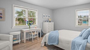 A bedroom with a bed, a desk, a chair, a dresser, and two windows with blinds. - The Sandpiper Private Deck Bay Boat Parking (Port Aransas)