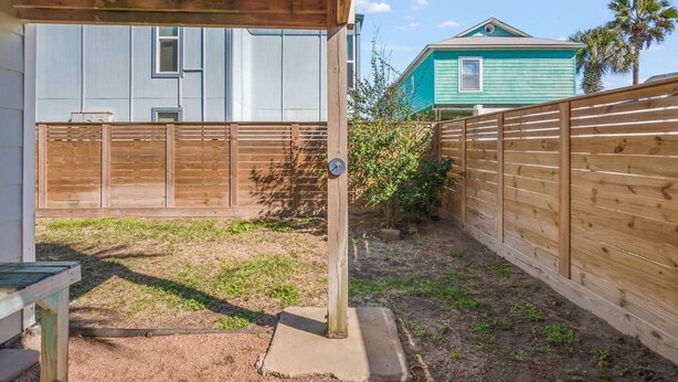 A fenced backyard with a covered patio area, a wooden fence, and a house in the background. - The Sandpiper Private Deck Bay Boat Parking (Port Aransas)