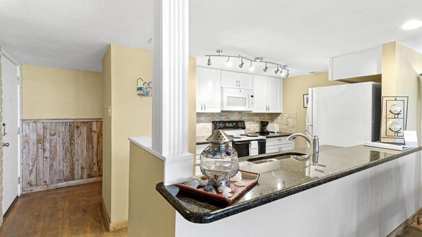 A kitchen with white cabinets, a granite countertop, and a stainless steel sink. - Sea Escape-boardwalk Access Large Community Pool (Port Aransas)
