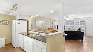 A modern kitchen with white cabinetry, a built-in island with a sink, and a dining area with a table and chairs. - Sea Escape-boardwalk Access Large Community Pool (Port Aransas)
