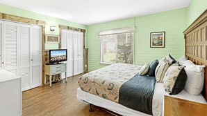 A bedroom with a bed, a television, a wardrobe, and a window with blinds. - Sea Escape-boardwalk Access Large Community Pool (Port Aransas)