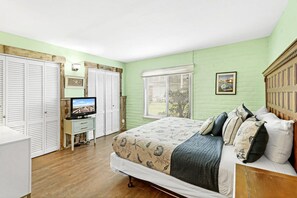 Ein Schlafzimmer mit Bett, Fernseher, Kleiderschrank und einem Fenster mit Jalousien.
