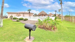 A residential area with a house, a barbecue grill, and a well-maintained lawn. - Sea Escape-boardwalk Access Large Community Pool (Port Aransas)